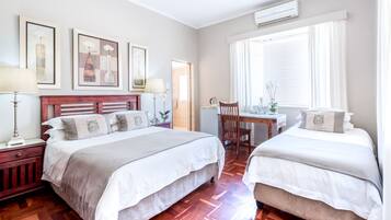 A hotel room with two beds, a wooden headboard, a desk with a chair, and framed artwork on the wall.