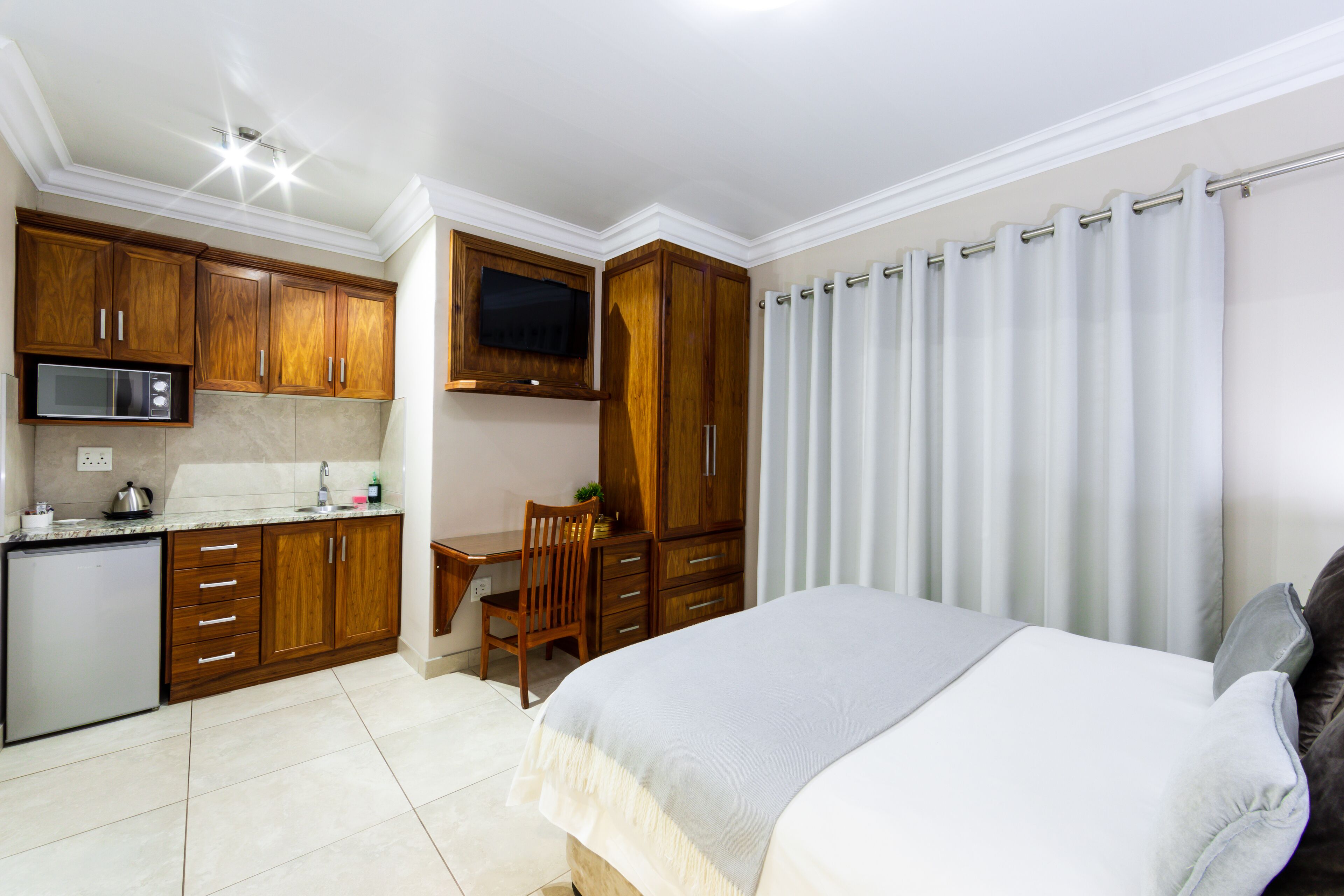 A compact bedroom with a bed, a desk, and a kitchenette.