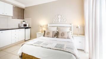A bedroom with a bed, nightstands, a dresser, and a microwave in the adjacent kitchen area.