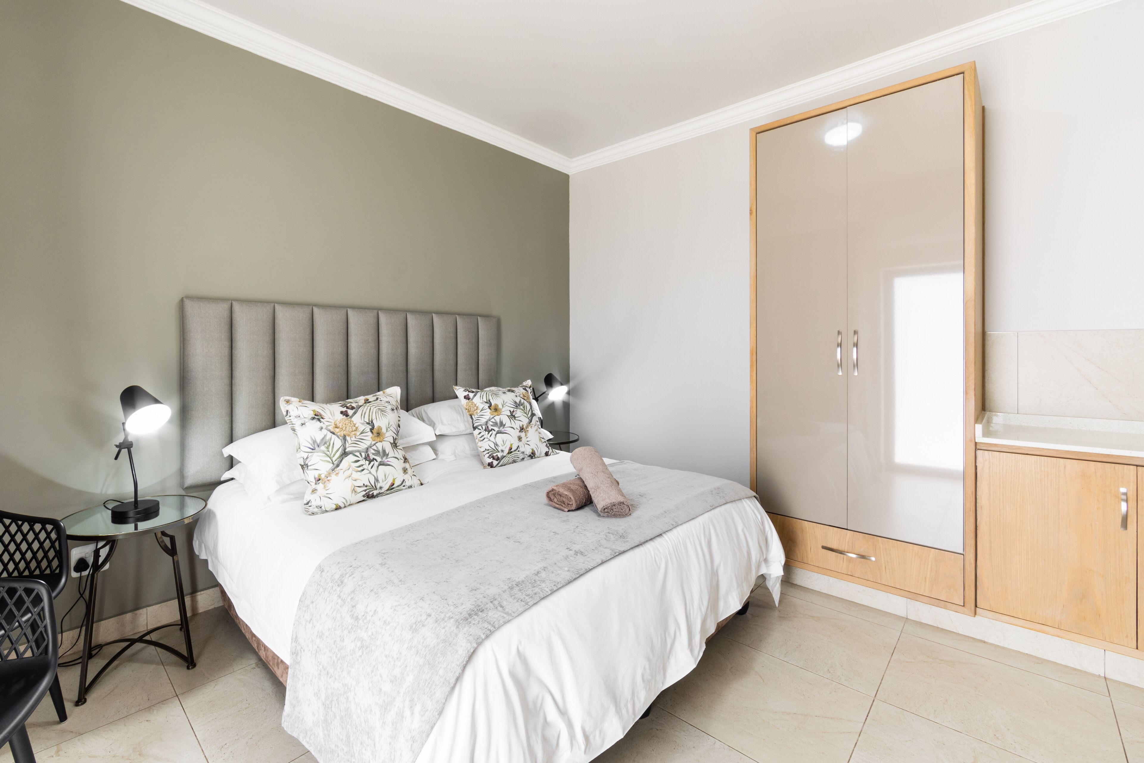 A bedroom with a bed, bedside tables, a wardrobe, and a small table with a lamp.