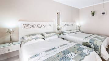 A bedroom with two beds, a nightstand with a lamp, a mirror, and two hanging birdcages.