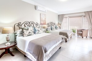 A hotel room with two beds, a chair, a lamp, and a window with curtains. - Adato Guesthouse (Potchefstroom)