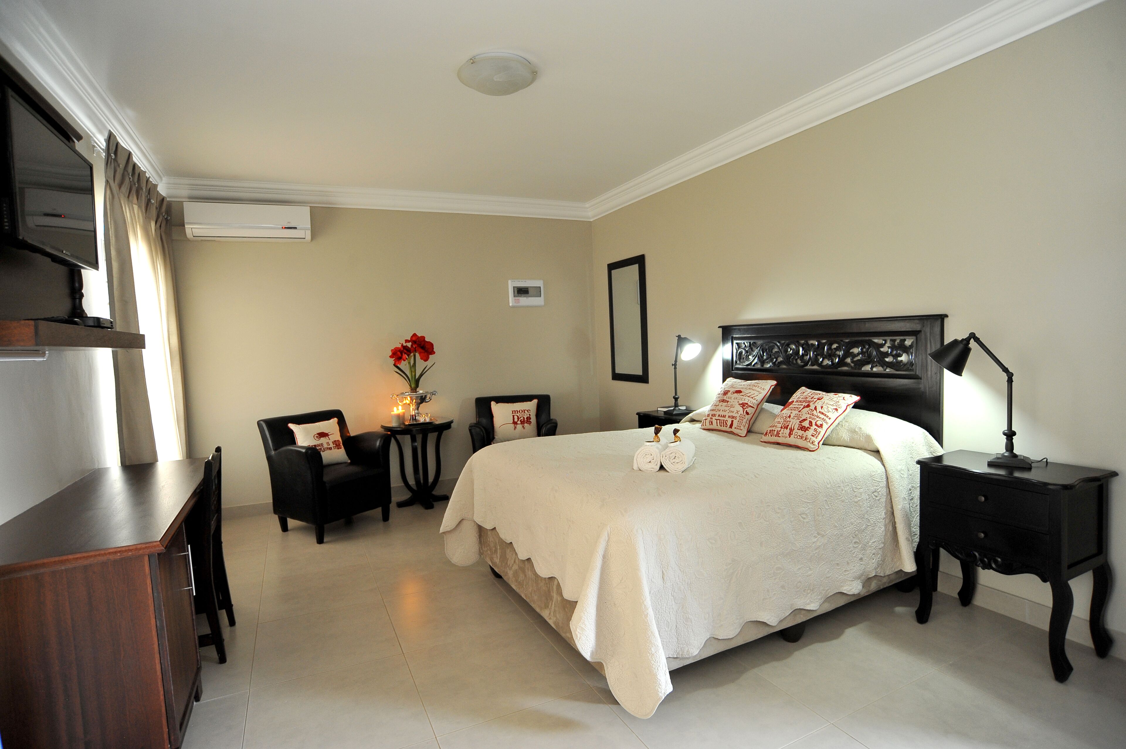 A neatly arranged bedroom with a large bed, a desk, a chair, and a small table with a vase of flowers.