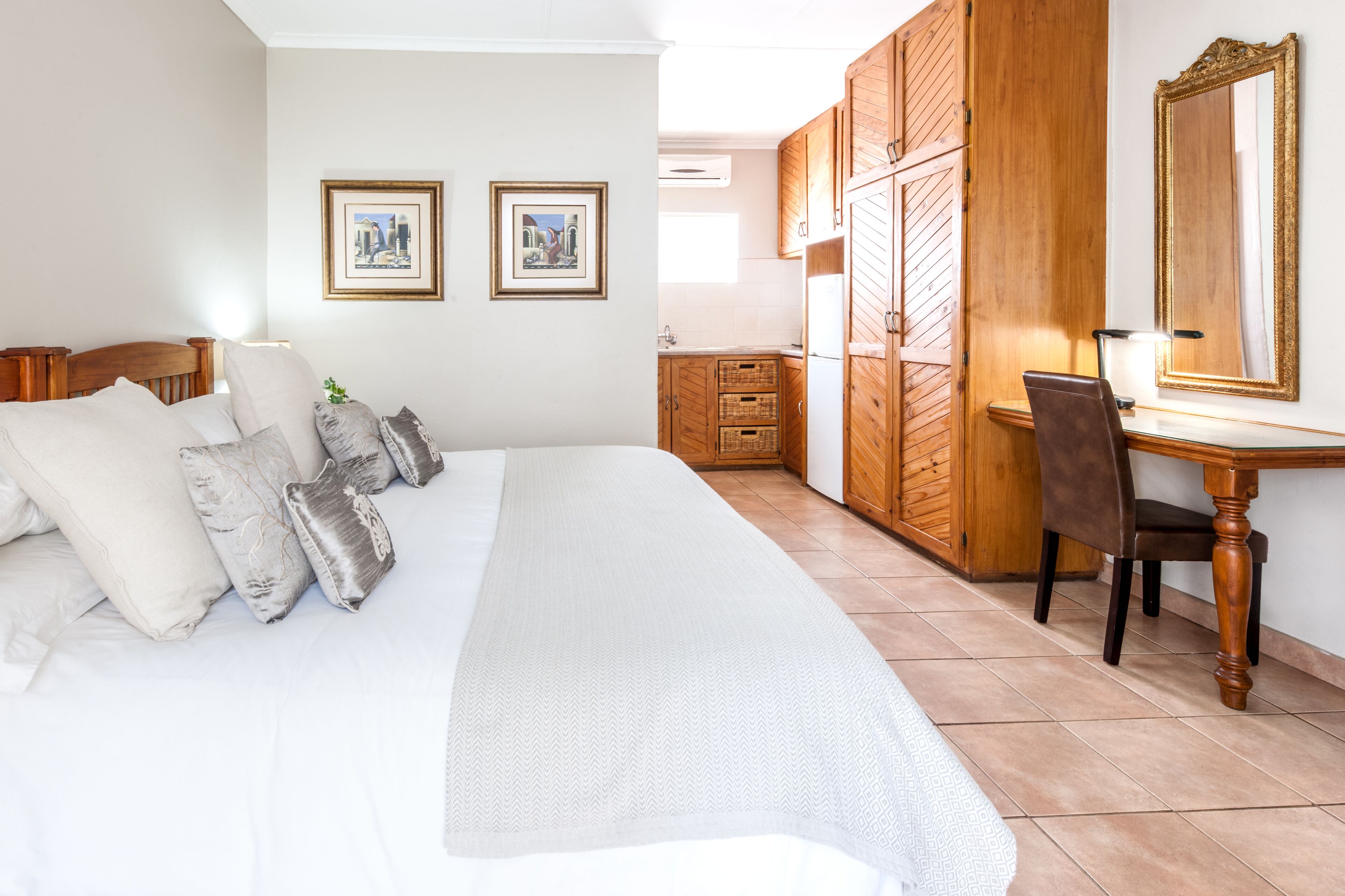 A bedroom with a bed, a desk, and a chair. There are two framed pictures on the wall.