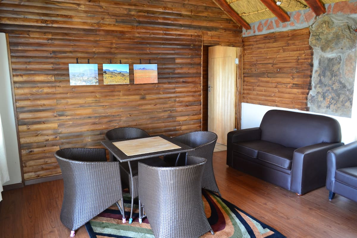A log cabin interior with a dining area, sofa, and wall-mounted pictures.
