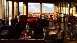Ein gemütliches Interieur mit Ledermöbeln, einem Holztisch mit einer Laterne und großen Fenstern mit Blick auf die Berge.