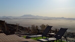 Eine Terrasse mit zwei Liegestühlen mit Blick auf eine gebirgige Landschaft.