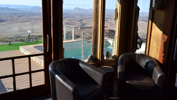 Ein Zimmer mit zwei Ledersesseln, Blick auf eine Berglandschaft und Poolbereich, durch das Fenster sichtbar.
