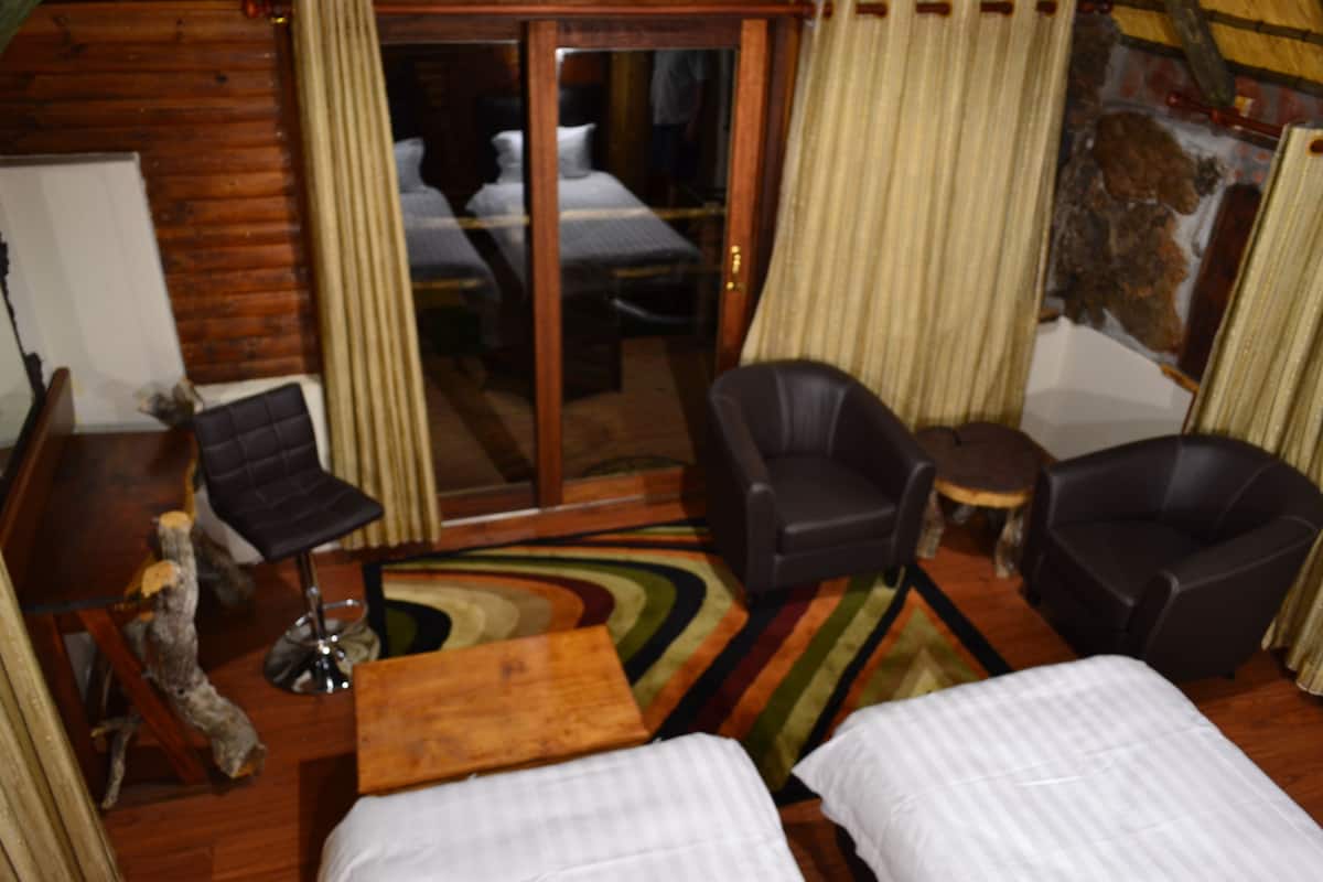 A room with two beds, a wooden floor, a glass door, and a view of a building outside.