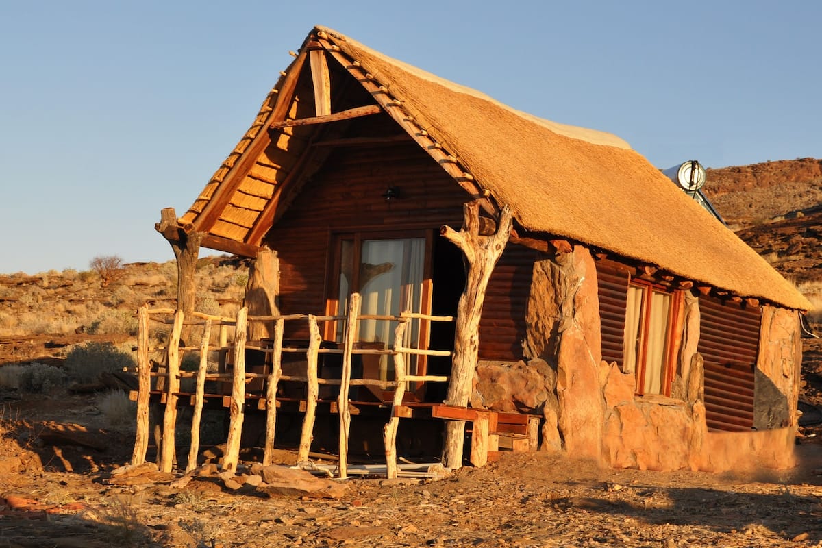 A rustic cabin with a thatched roof, wooden walls, and a wooden fence.