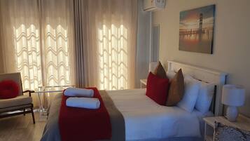 Een hotelkamer met een bed, een stoel, een rood kussen, een witte lamp en een schilderij aan de muur.