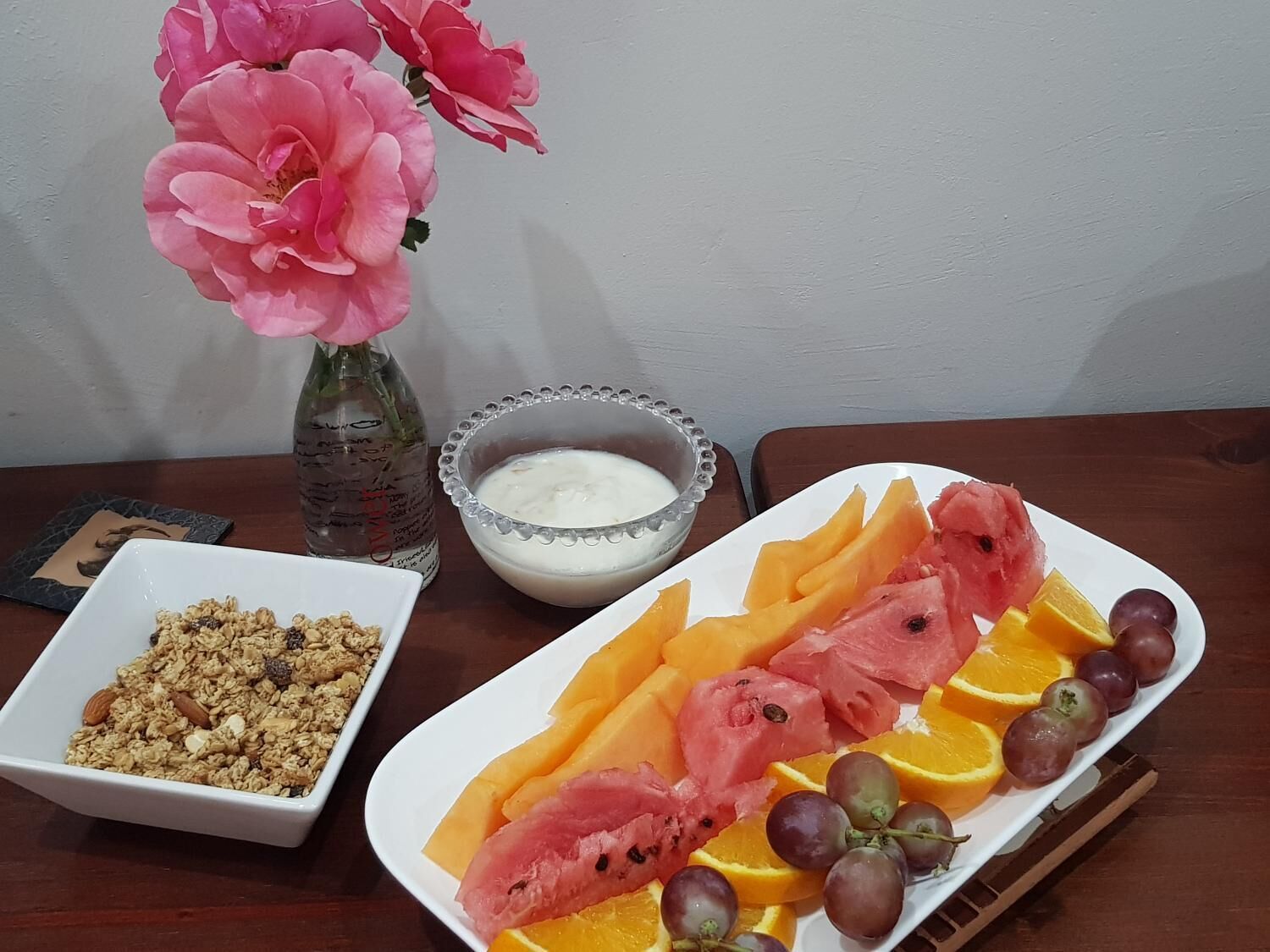Una mesa con un plato de fruta, un bol de yogur y un bol de granola.
