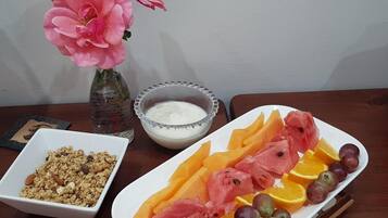 Una mesa con un plato de fruta, un bol de yogur y un bol de granola.