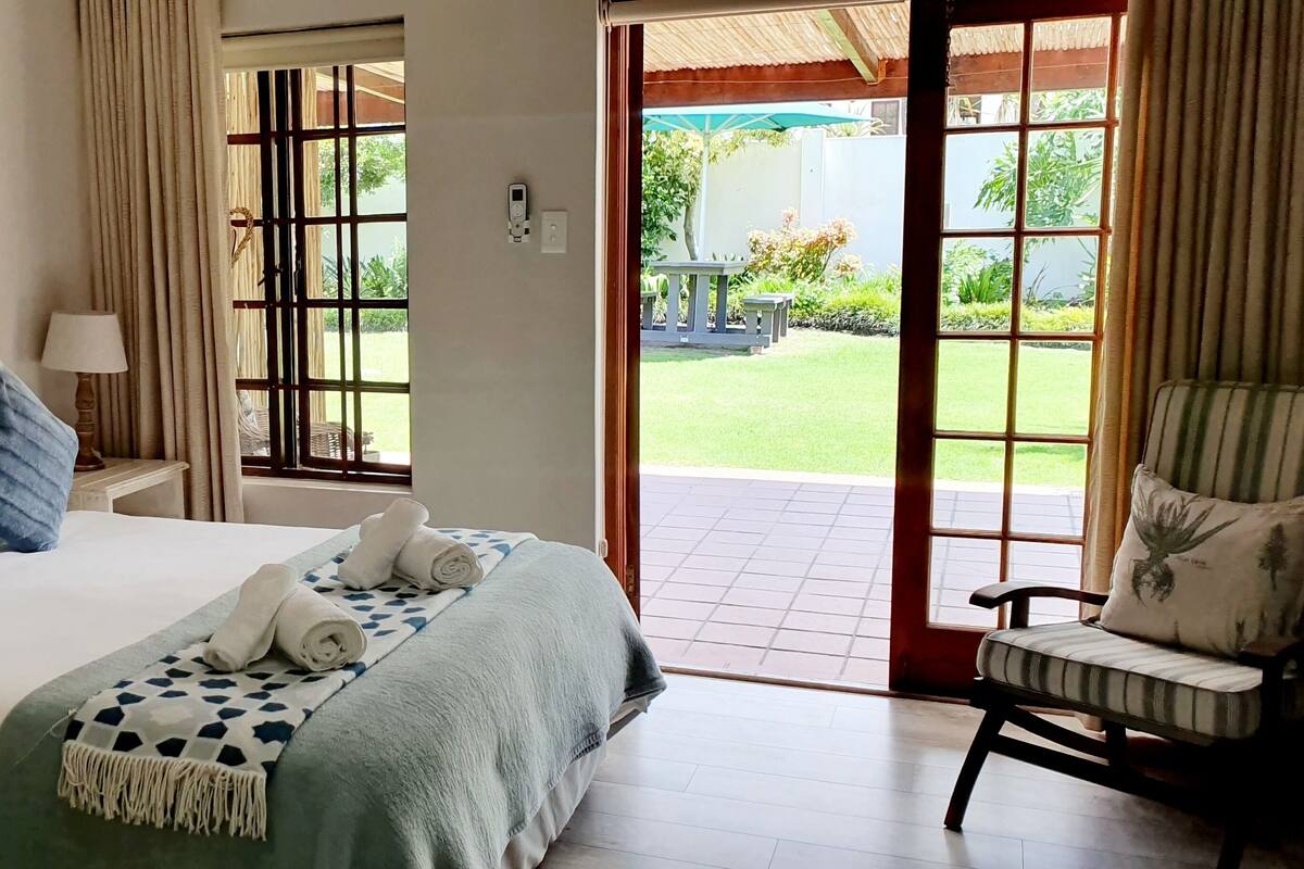 A hotel room with a bed, a chair, a painting, and a view of the outdoors.