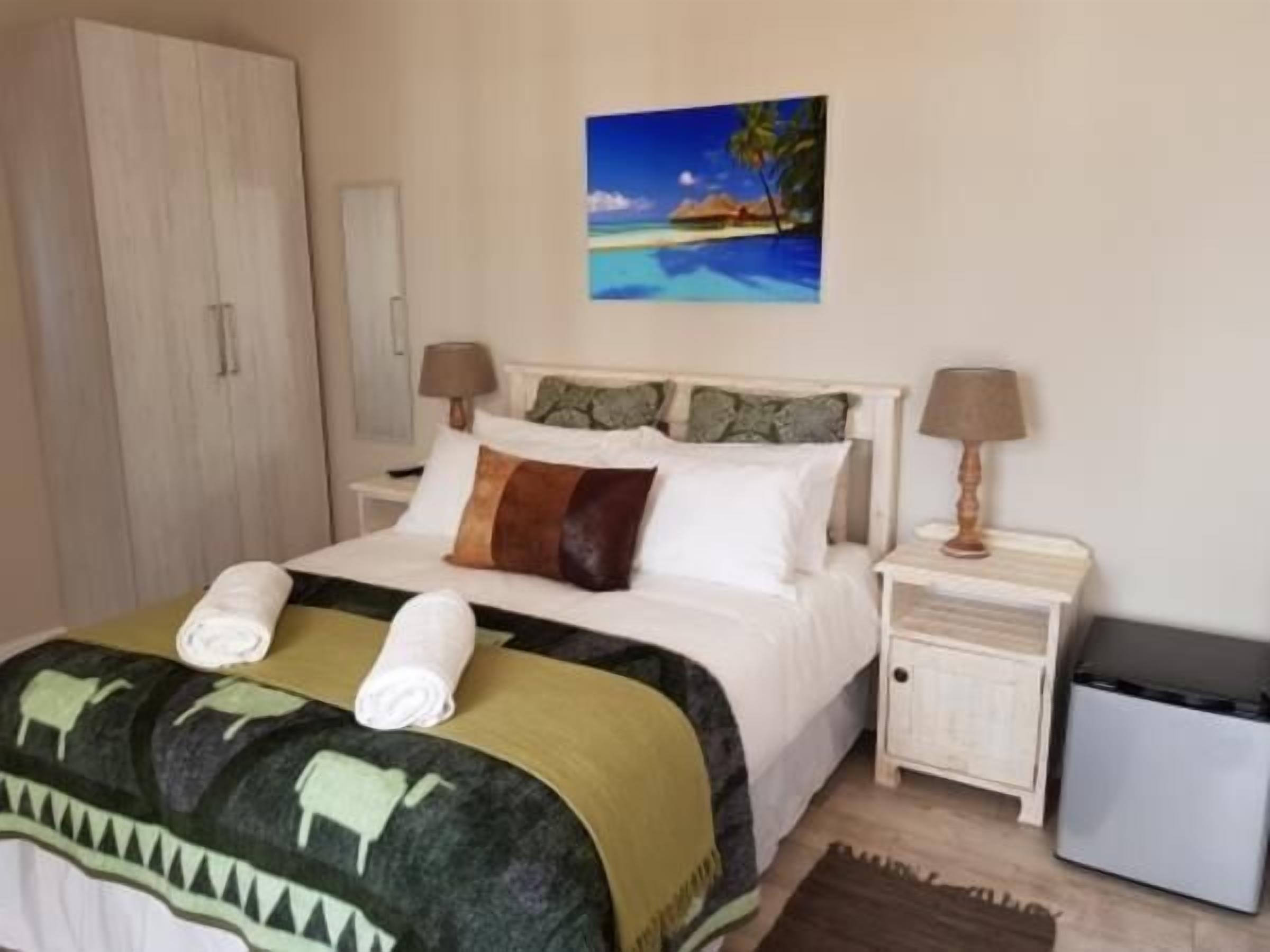 A neatly arranged hotel room with a bed, a nightstand, a wardrobe, and a painting of a beach scene.