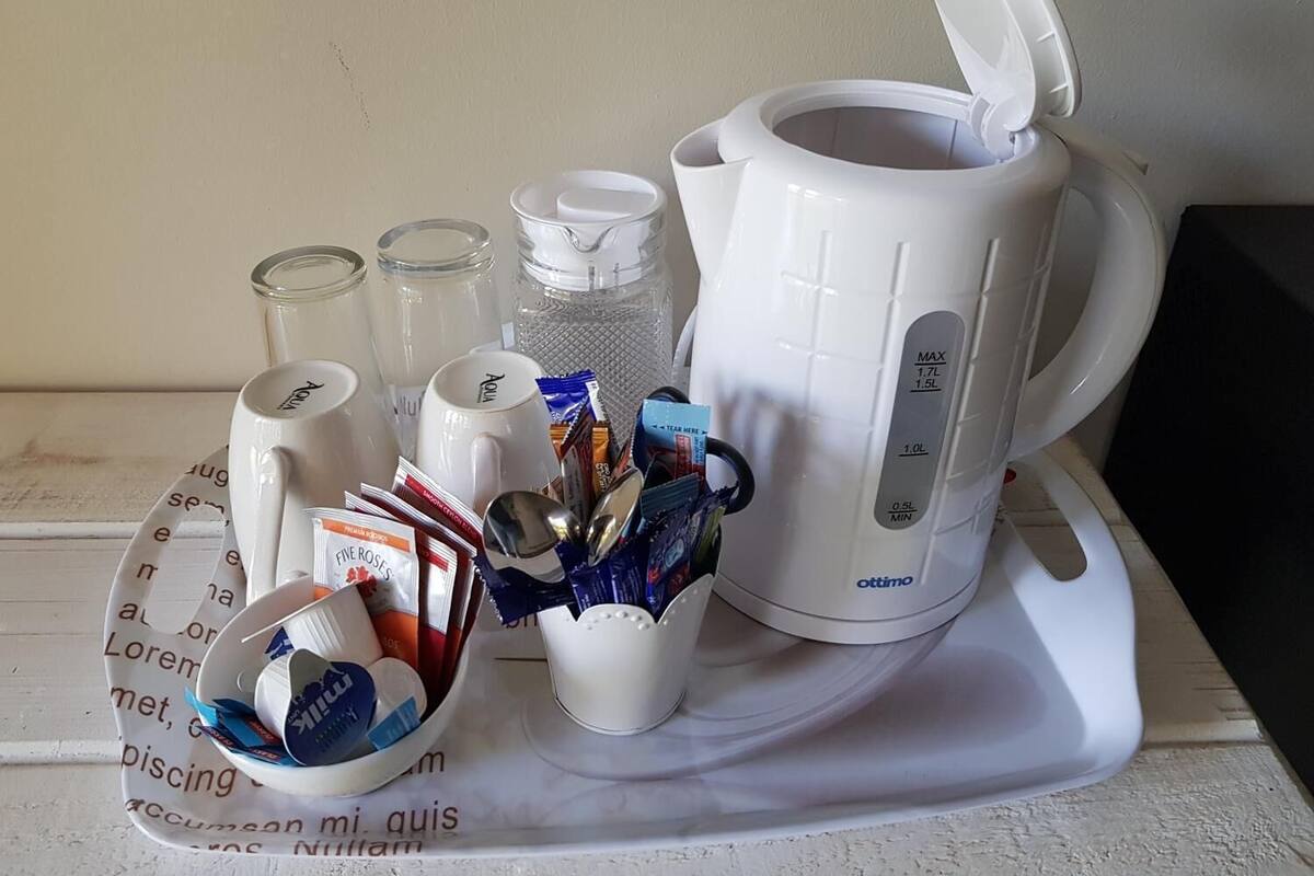 A white coffee maker with a capacity of 1.7L and 1.5L, a white mug, a glass jar, and a white cup with a spoon.