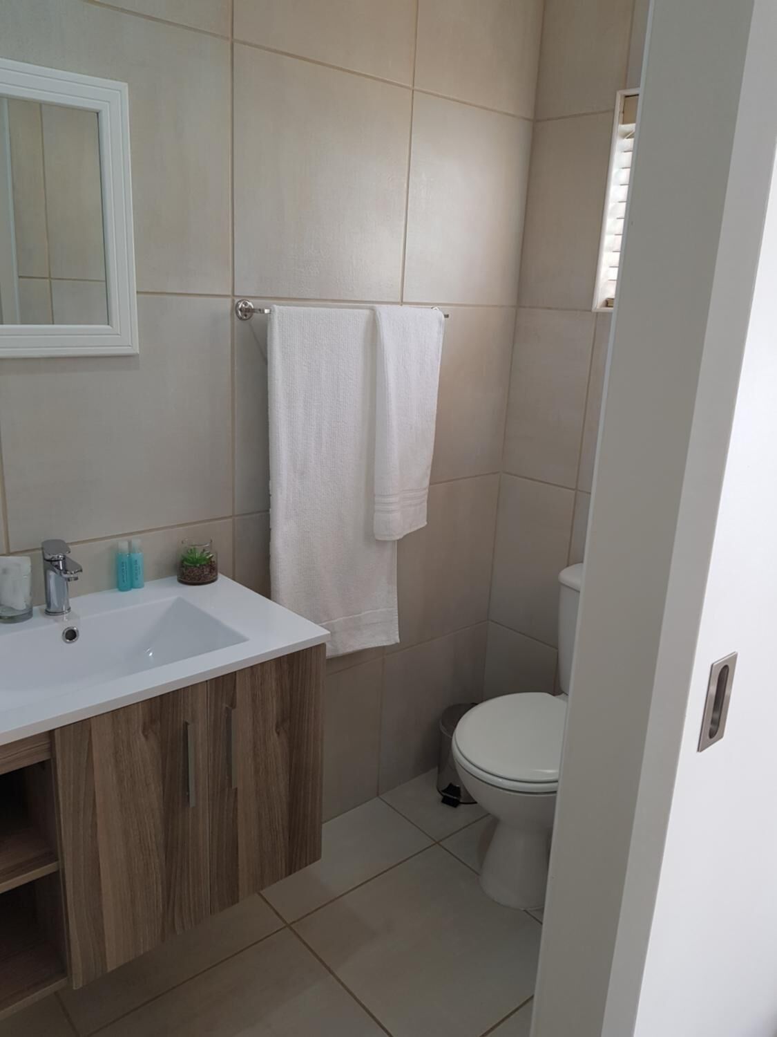 A bathroom with a white sink, wooden vanity, two white towels, and a toilet.