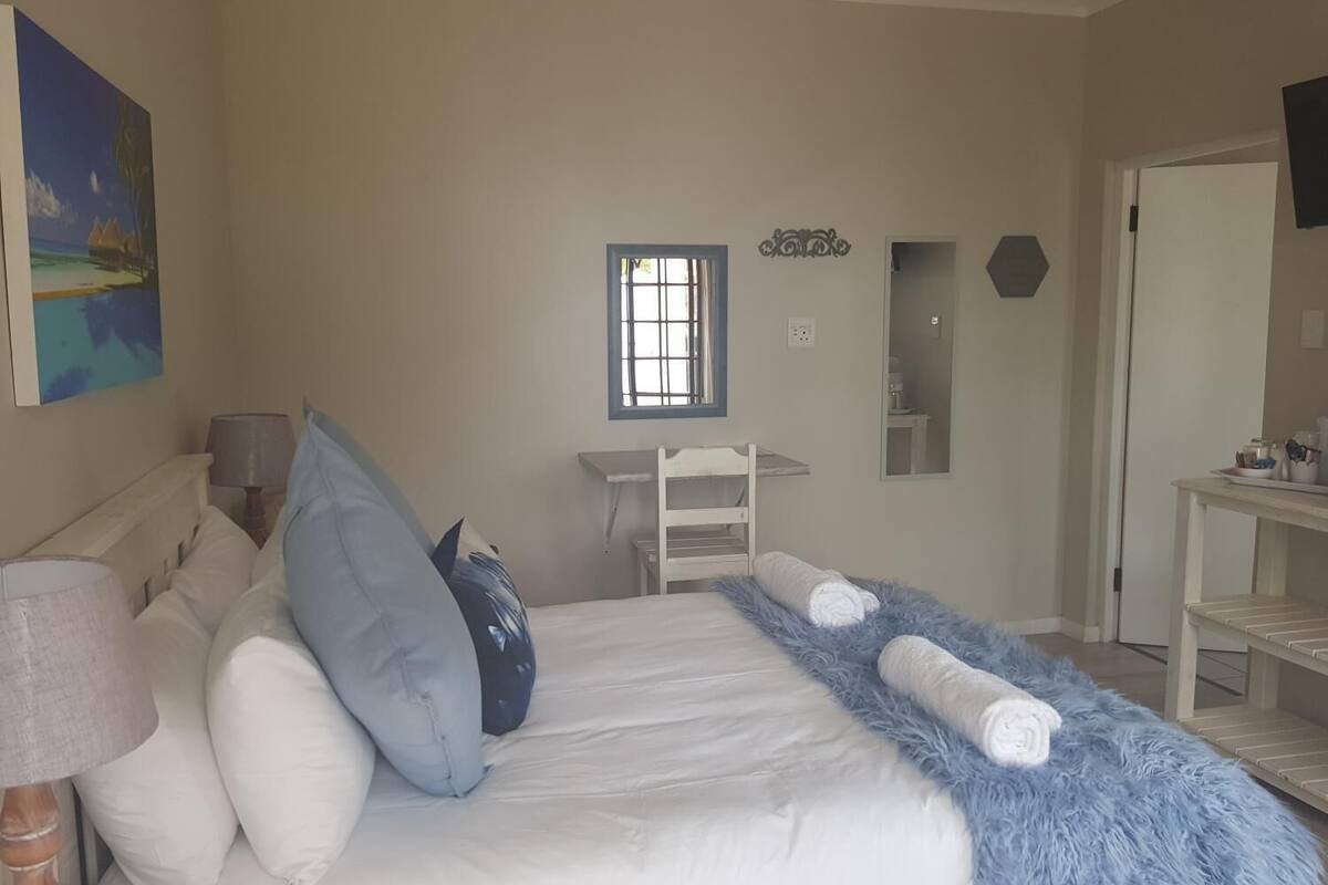 A bedroom with a bed, pillows, a desk, a chair, a window, and a mirror.