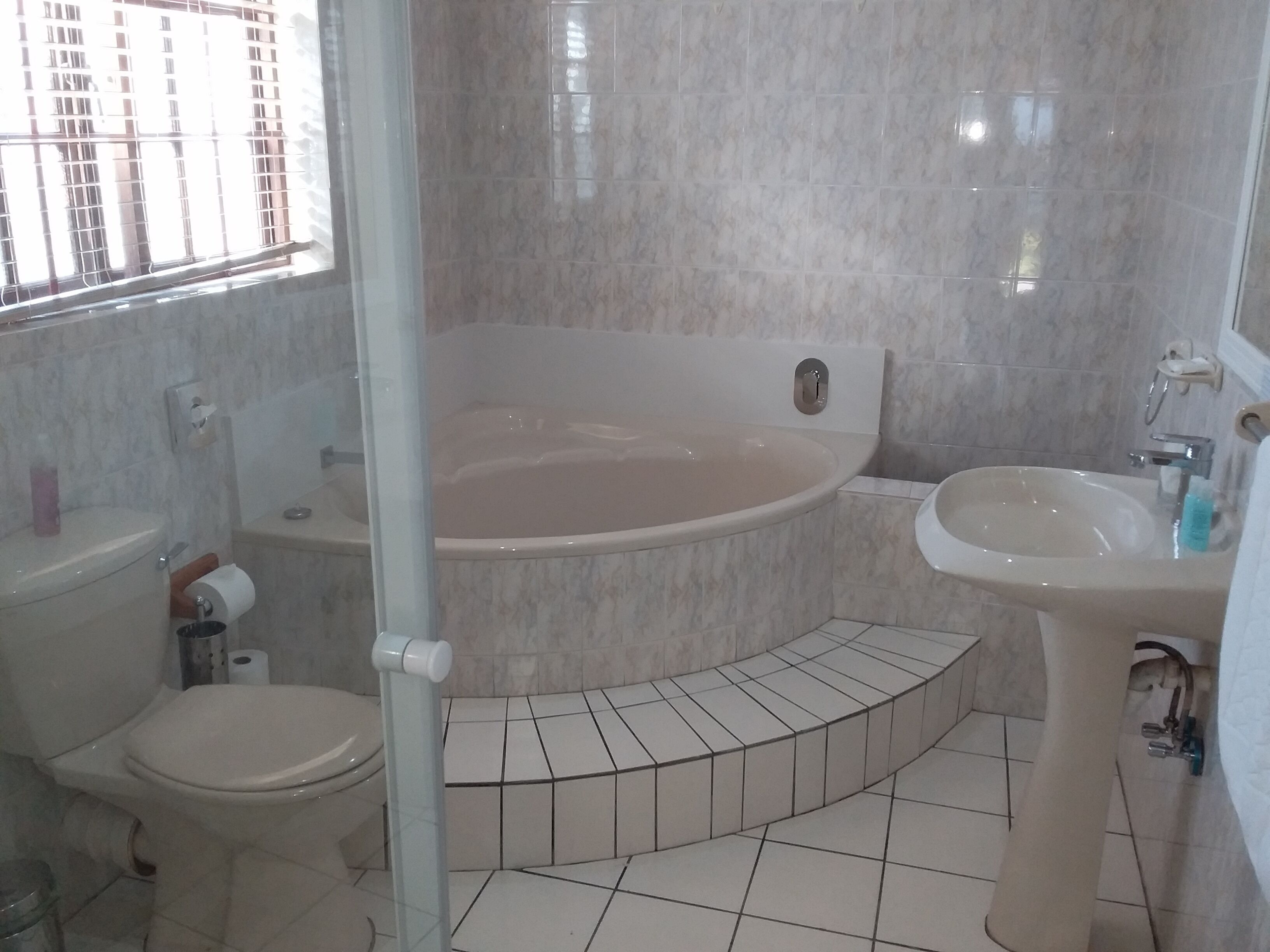 A bathroom with a bathtub, toilet, and sink, featuring tiled flooring and a window with a view of buildings.