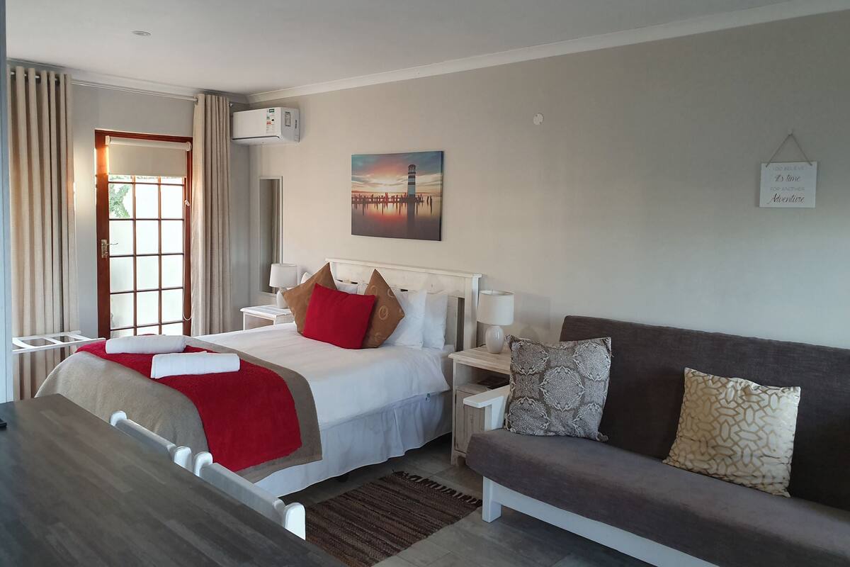 A hotel room with a bed, bedside tables, a sofa, a painting, and a motivational sign.