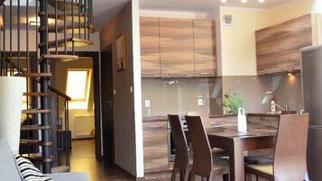 A spacious living area with a staircase leading to a loft, a dining area with a table and chairs, and a kitchen with wooden cabinets.