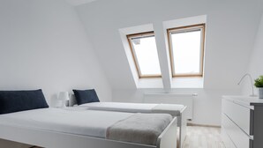 Un dormitorio moderno con dos camas, un escritorio pequeño y una ventana.