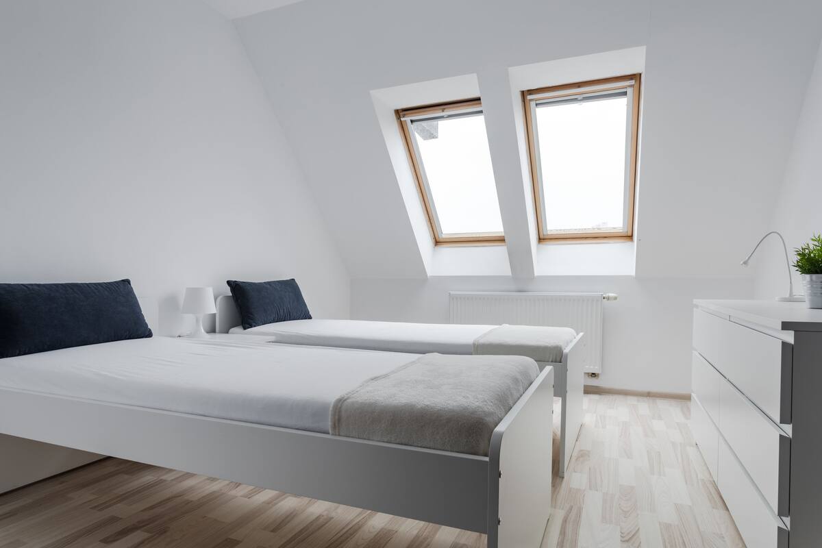 A modern bedroom with two beds, a small desk, and a window.