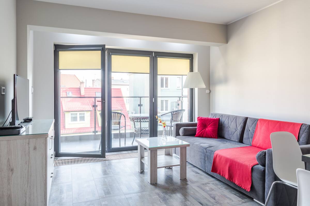 A modern living room with a grey sofa, red throw, and a glass coffee table.