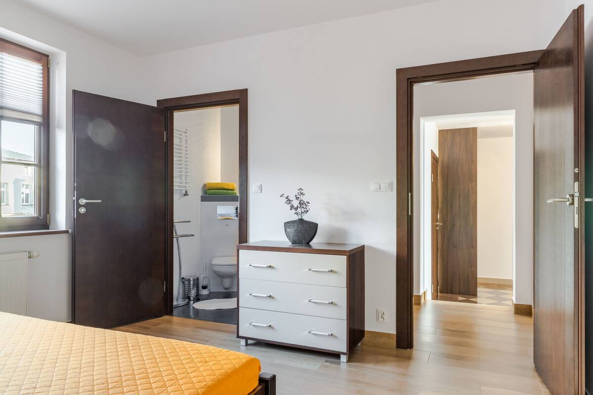 A bedroom with a bed, a dresser, and a bathroom visible through an open door.