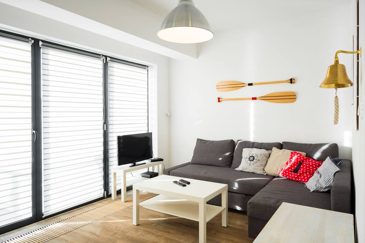 A modern living room with a grey sofa, a white coffee table, a TV, and a sliding glass door.