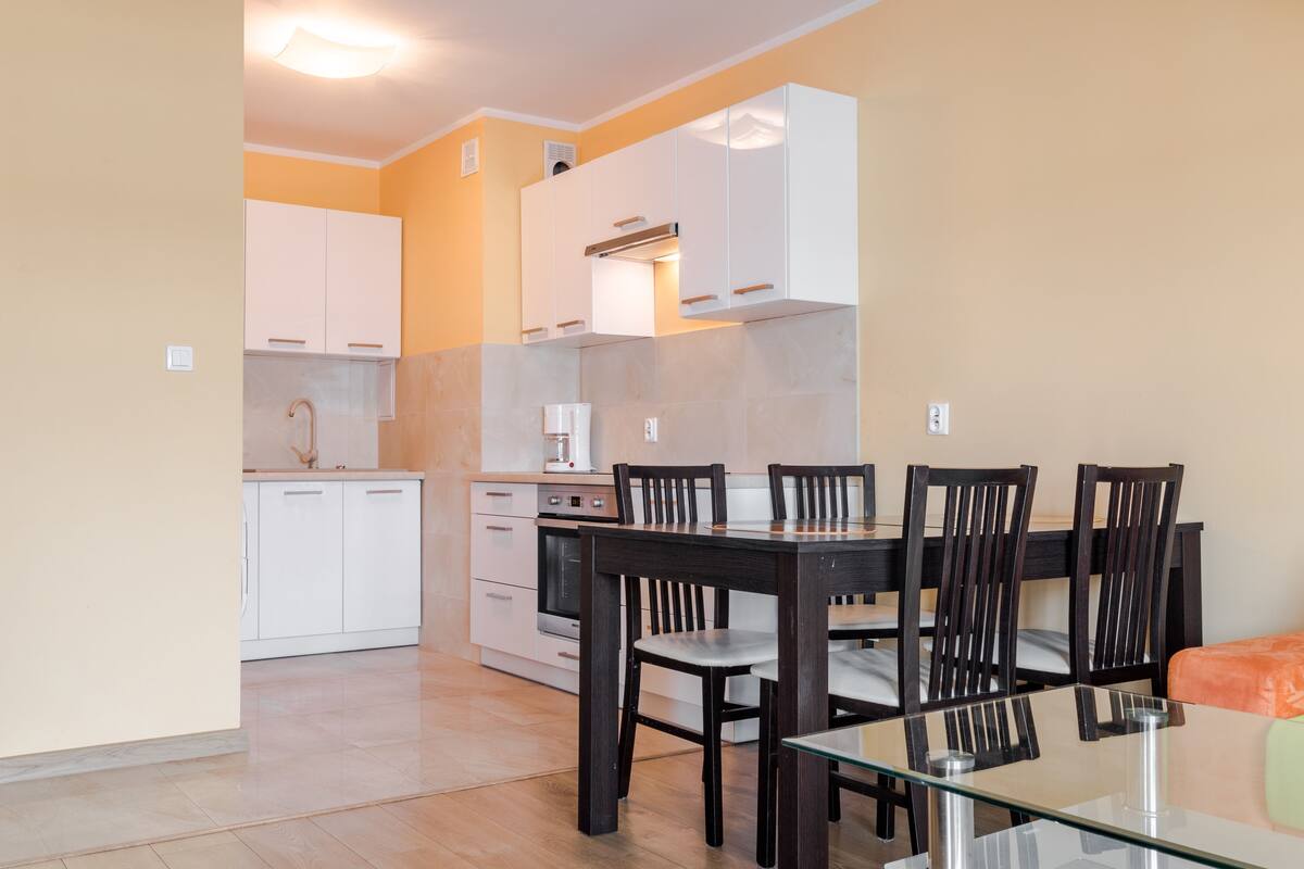 A modern kitchen with white cabinets, a glass dining table, and wooden chairs.