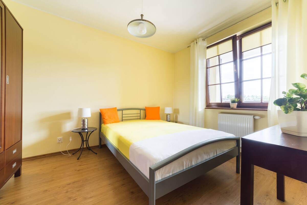 A bedroom with a bed, bedside tables, a wardrobe, a window with curtains, and a potted plant.