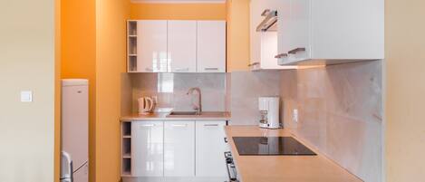 Une cuisine de taille réduite avec des meubles blancs, un évier, une cuisinière et une machine à café.