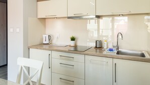 Una cocina moderna con armarios blancos, un lavamanos de acero inoxidable y una cafetera.