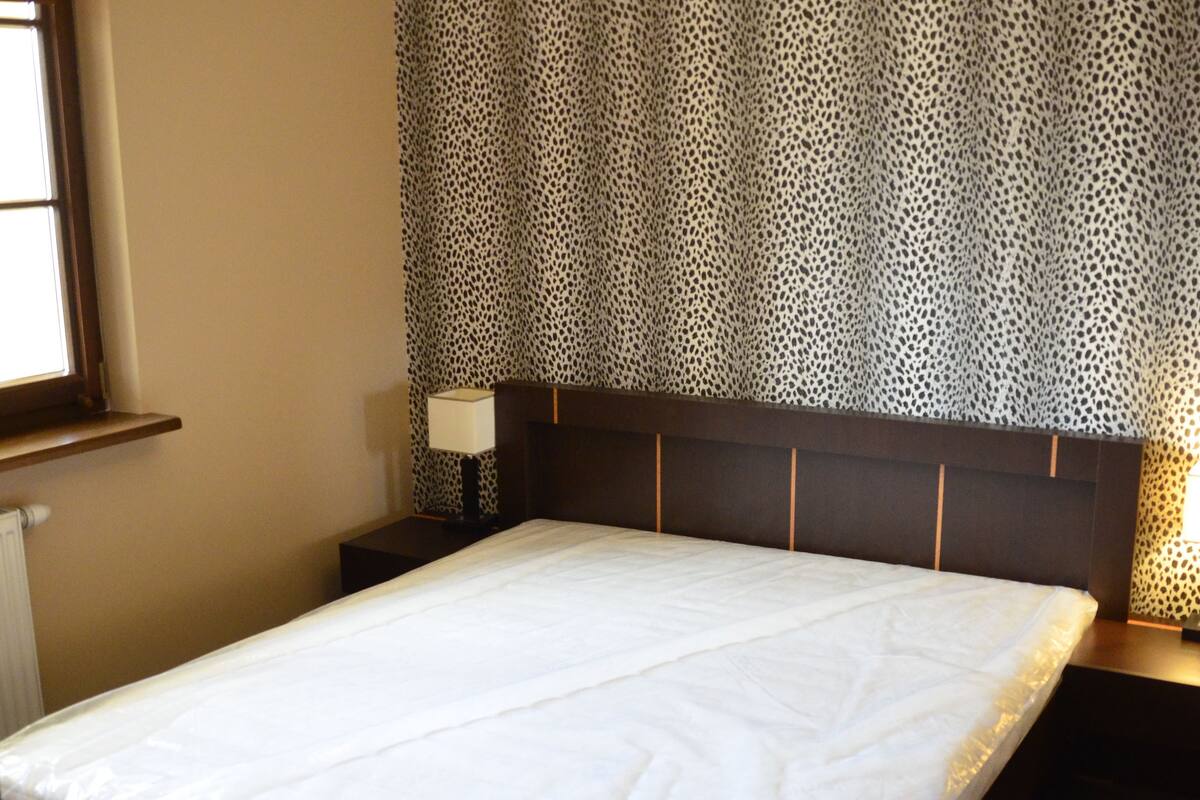 A neatly made bed with a headboard, a bedside lamp, and a patterned wallpaper.