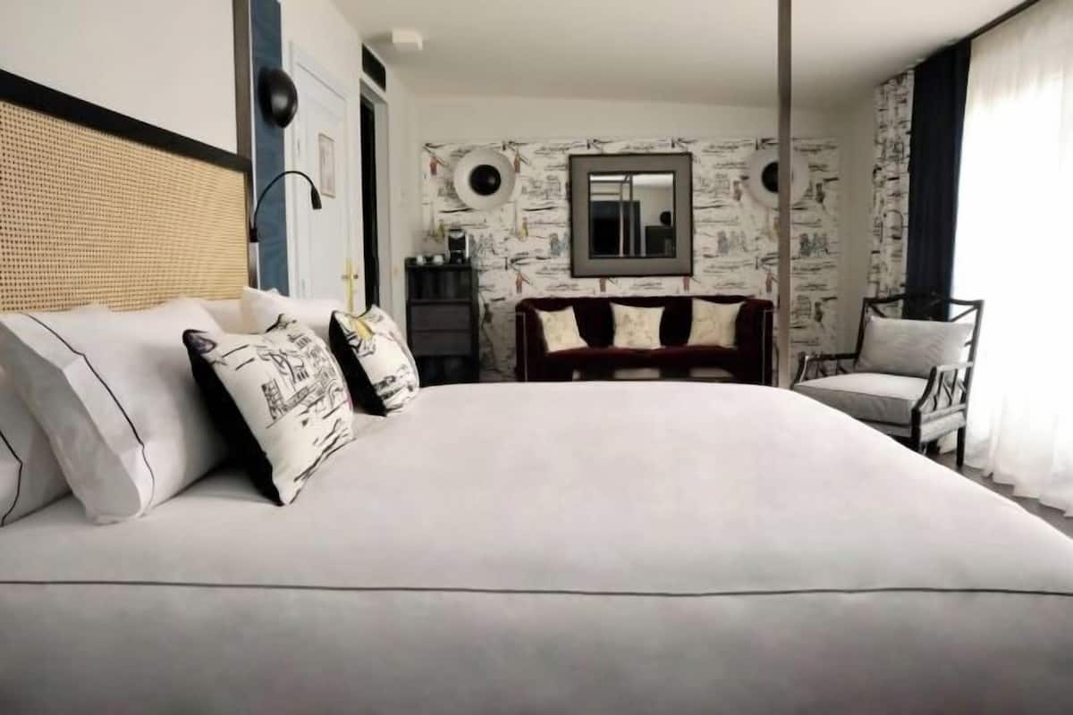 Une chambre à coucher avec un grand lit, un canapé, un fauteuil, un miroir et un mur orné d’un motif circulaire.