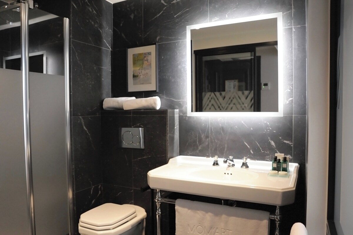 A modern bathroom with a white toilet, a sink with a mirror above it, and a towel hanging on the wall.