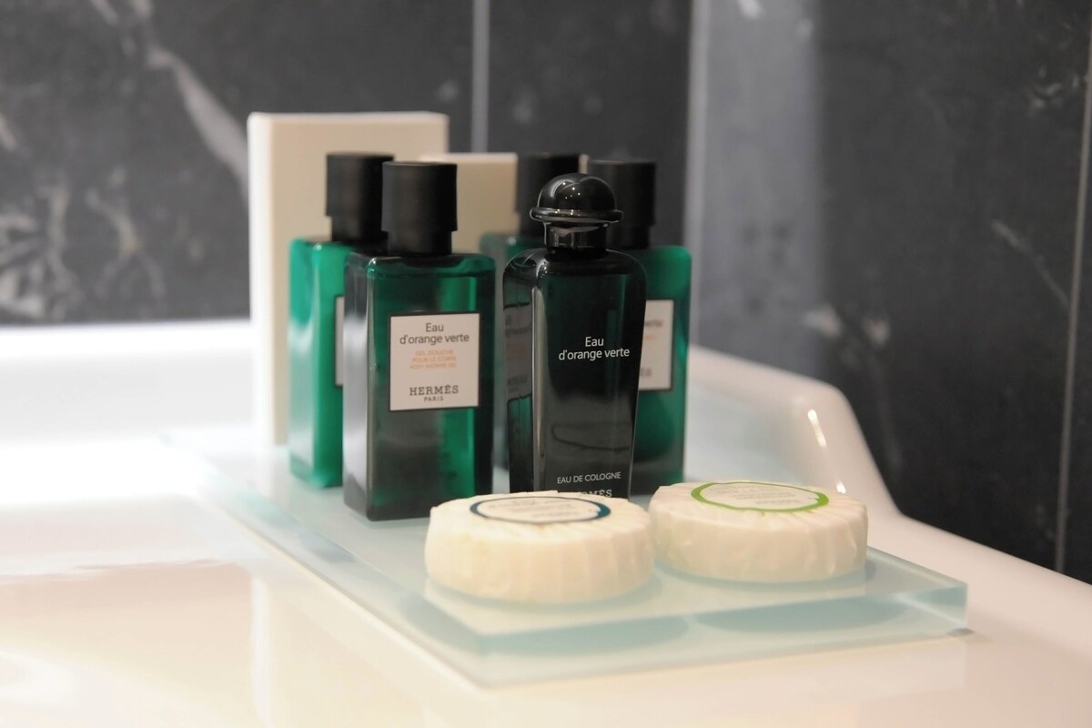 A bathroom with a white sink, green and black bottles of perfume, and two white soap bars on a clear tray.