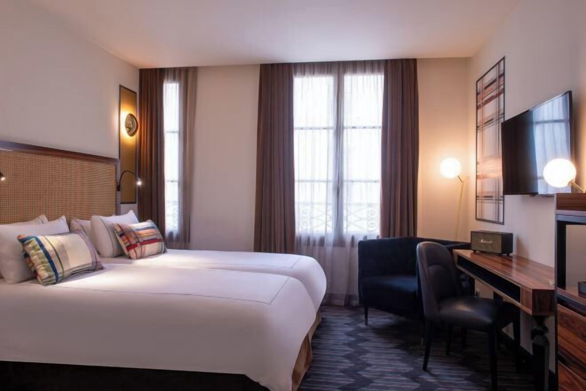 A hotel room with a large bed, a desk, a chair, a television, and a window with curtains.