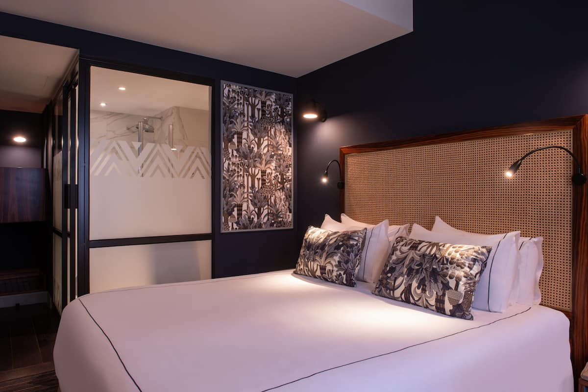 Une chambre à coucher moderne avec un grand lit, une tête de lit ornée d’un motif tissé et des œuvres d’art accrochées aux murs.