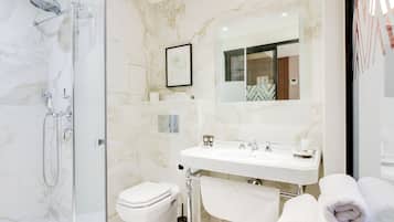 Une salle de bain moderne avec une douche à parois de verre, des toilettes blanches, un lavabo avec un miroir au-dessus et deux serviettes enroulées posées sur le sol.