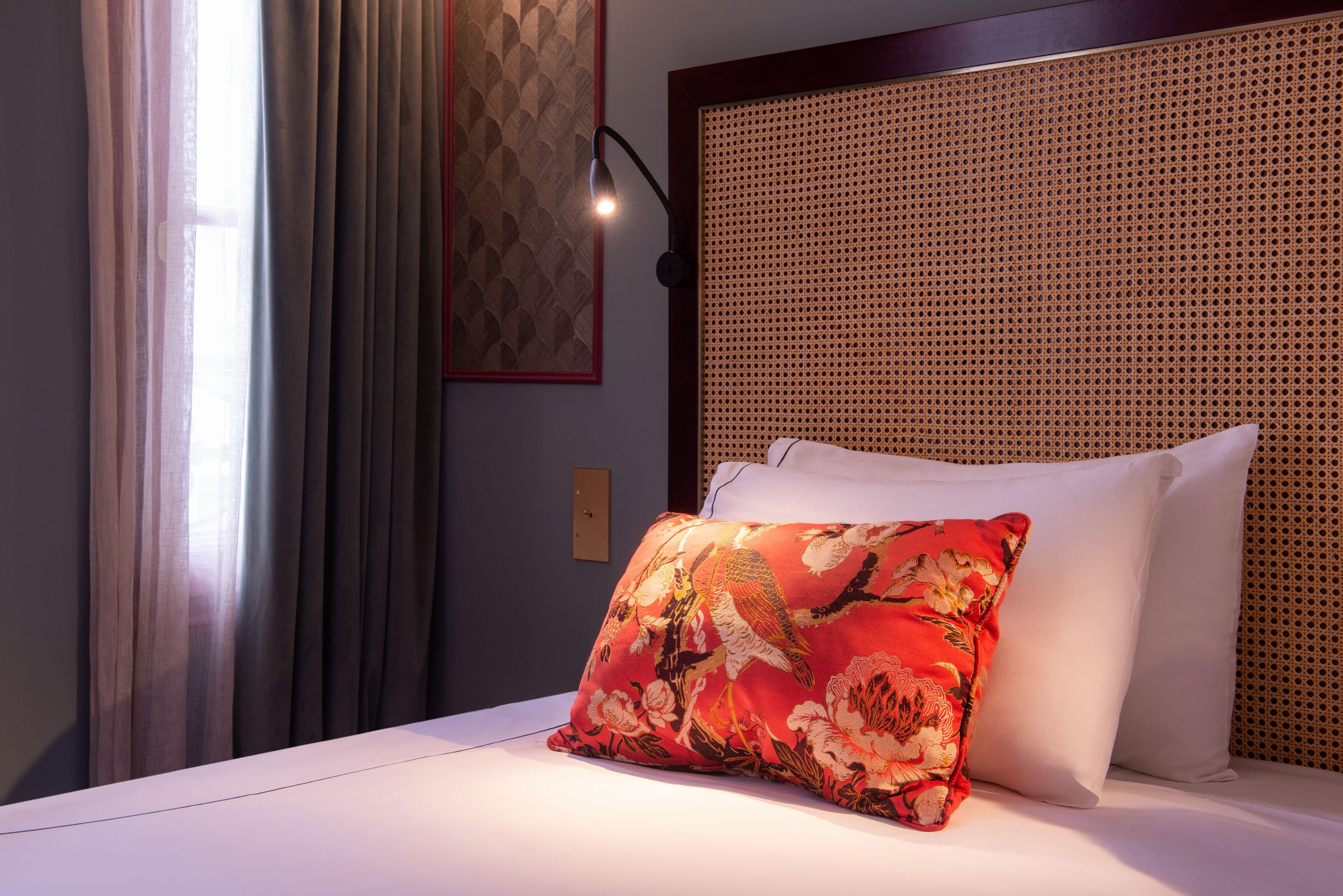 Una cama bien hecha con sábanas blancas, una almohada de flores rojas y un cabecero con diseño tejido.