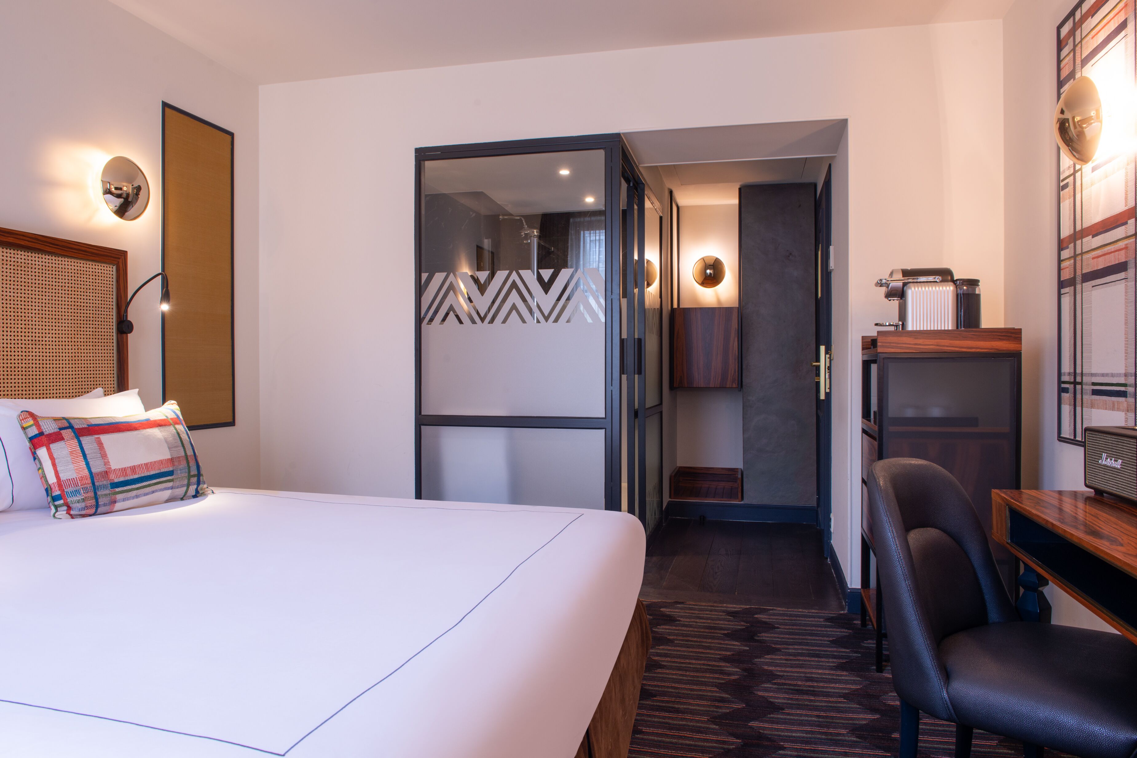 A hotel room with a bed, a desk, a chair, a mirror, and a door leading to a bathroom.