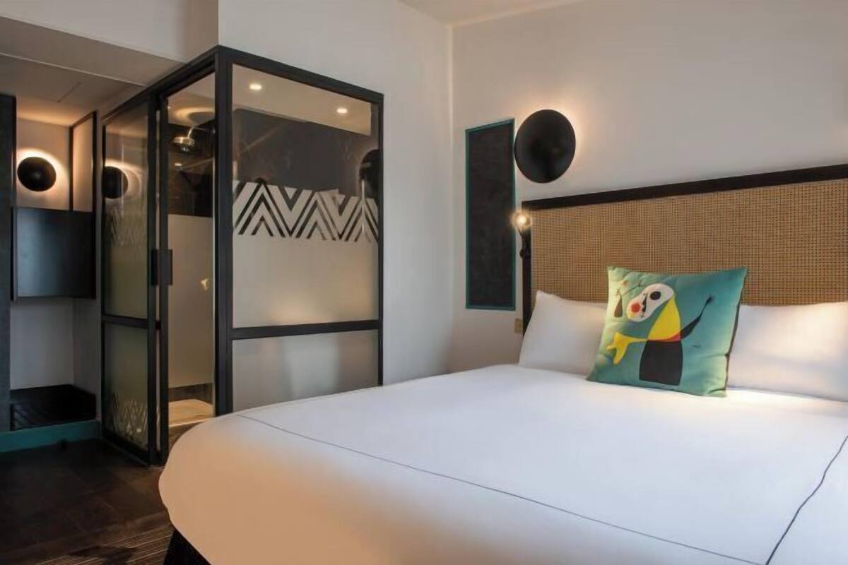 Une chambre d’hôtel moderne avec un grand lit, une cloison en verre et un coussin décoratif.