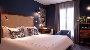 A hotel room with a large bed, a desk, a chair, and a bookshelf. - Mom’Art Hotel (Paris)