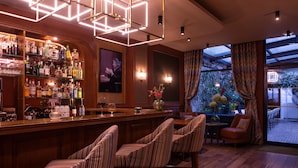 A bar area with wooden bar stools, a variety of liquor bottles, and a television screen. - Mom’Art Hotel (Paris)