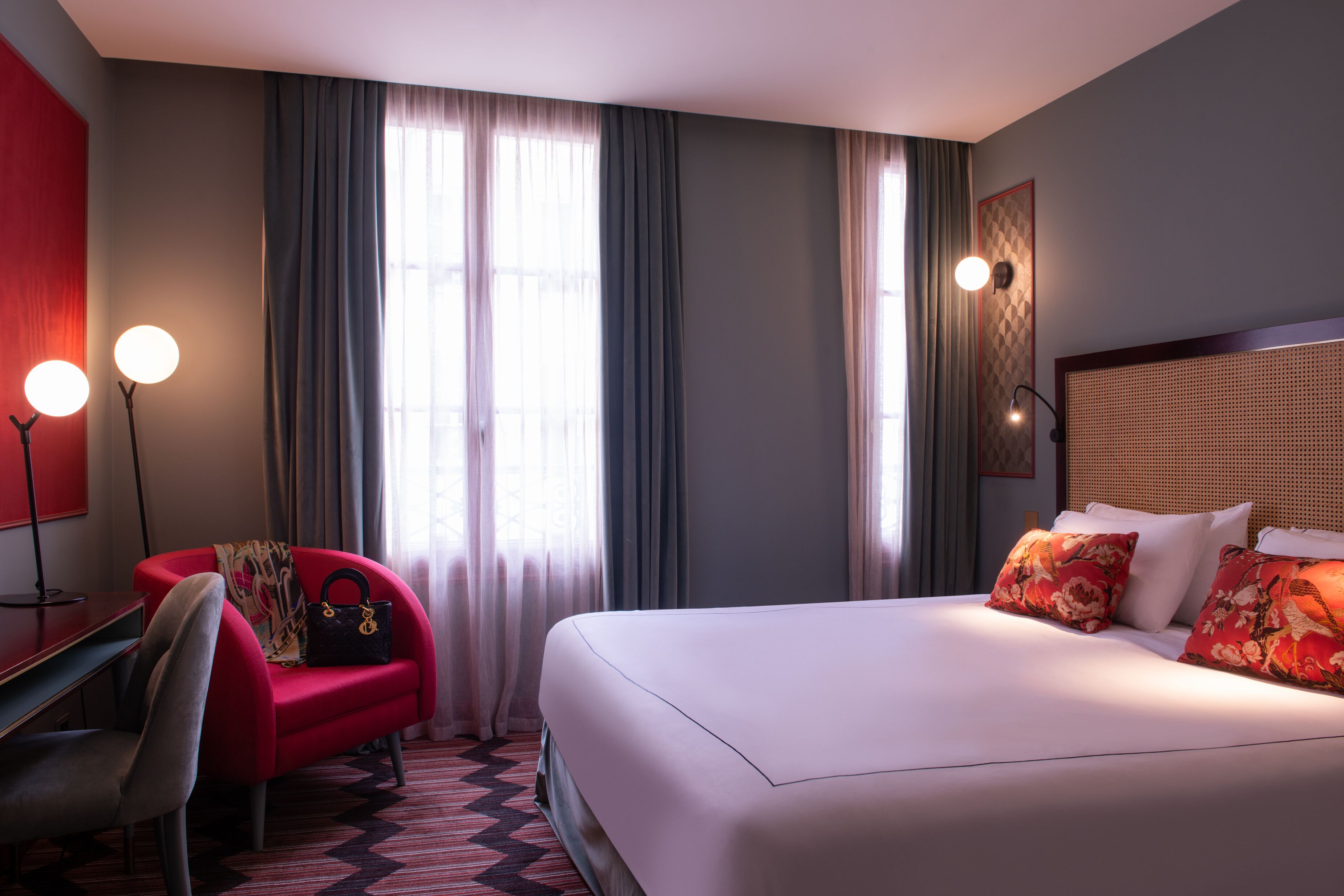 A hotel room with a bed, a desk, a chair, and a red armchair.