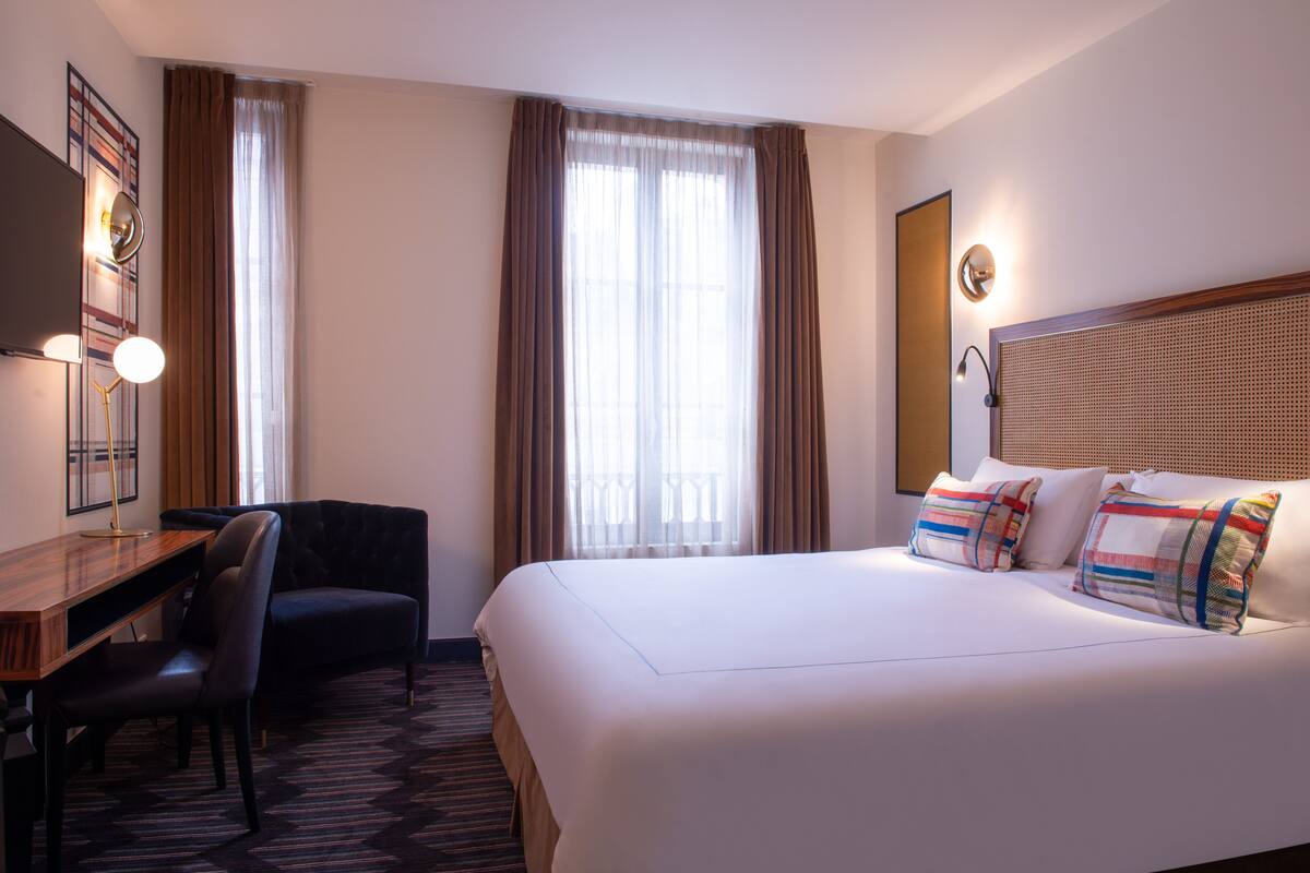 Une chambre d’hôtel avec un grand lit, un bureau, une chaise et une fenêtre avec des rideaux.