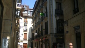 Una calle estrecha flanqueada por edificios, algunos con balcones y señalización que indica restaurantes.