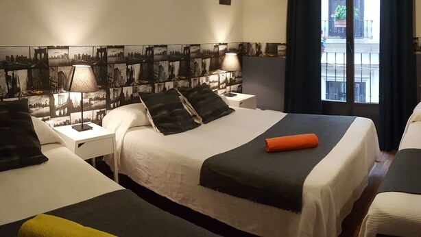 Habitación de hotel con dos camas, una mesita de noche, una lámpara y vistas a la ciudad desde la ventana.